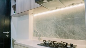 A modern kitchen with a white countertop, a gas stove, a sink, and a backsplash with a marble-like texture. - Homey And Cozy Stay Studio Belmont Residence Puri Apartement (Jakarta)