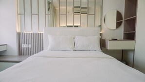 A modern hotel room with a large bed, a bedside table, a mirror, and a built-in wardrobe. - Homey And Cozy Stay Studio Belmont Residence Puri Apartement (Jakarta)