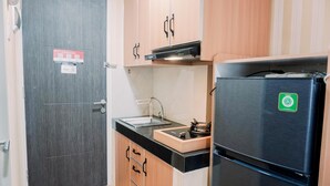 A compact kitchen with a dark door, wooden cabinets, a stainless steel refrigerator, and a sink.