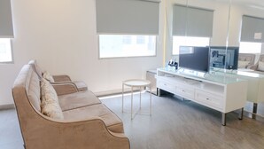 Un salon moderne avec un canapé beige, un bureau à plateau en verre, un téléviseur à écran plat et un grand miroir.