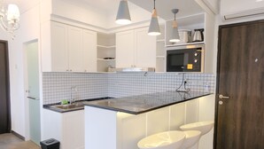 Une cuisine moderne avec des armoires blanches, un comptoir noir et un four encastré. On y trouve trois luminaires suspendus et un petit îlot central avec des tabourets de bar.
