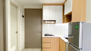 A compact kitchen with a built-in gas stove, a stainless steel refrigerator, wooden cabinets, and a white tiled backsplash. - Great Deal And Pleasurable 2Br Vasanta Innopark Apartment (Cikarang)