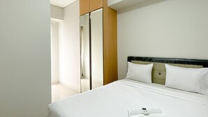 A hotel room with a large bed, a wooden wardrobe, and a mirror. - Great Deal And Pleasurable 2Br Vasanta Innopark Apartment (Cikarang)