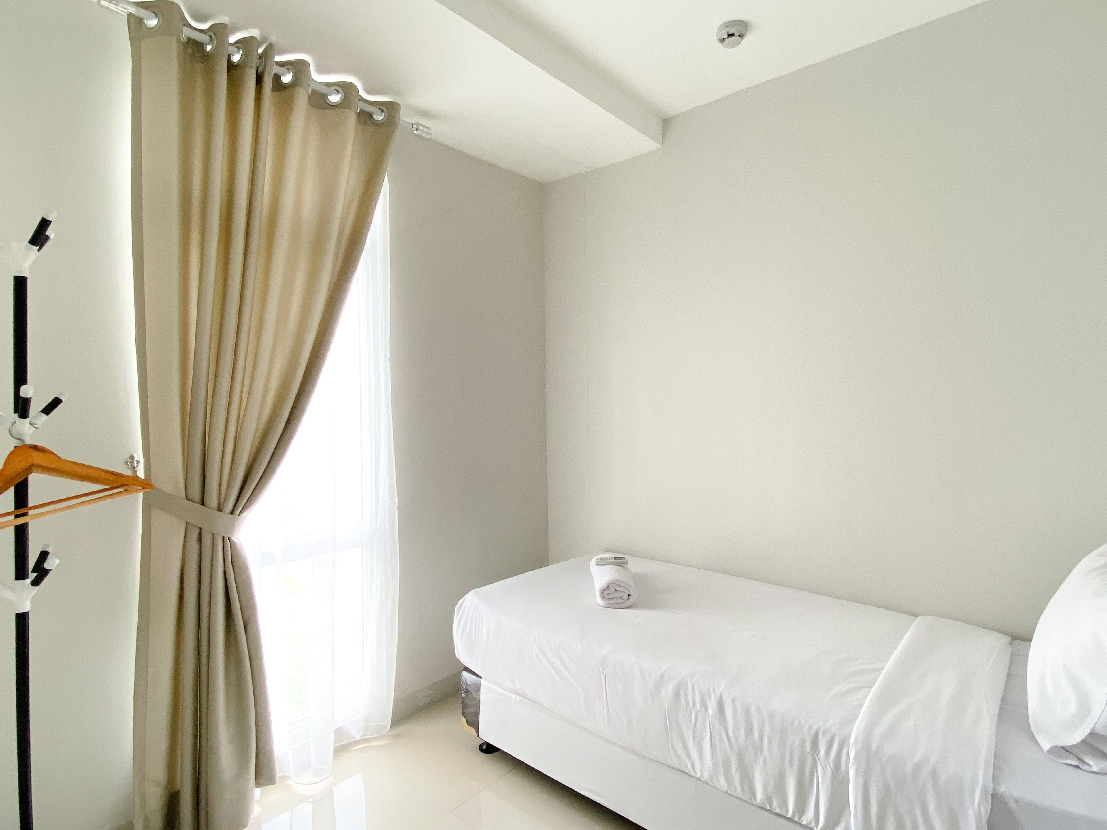 Une chambre à coucher au style minimaliste, avec un lit, un porte-manteau suspendu et une fenêtre avec des rideaux.