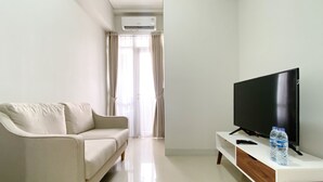 A modern living room with a sofa, a flat-screen TV, a water bottle, and an air conditioning unit. - Great Deal And Pleasurable 2Br Vasanta Innopark Apartment (Cikarang)
