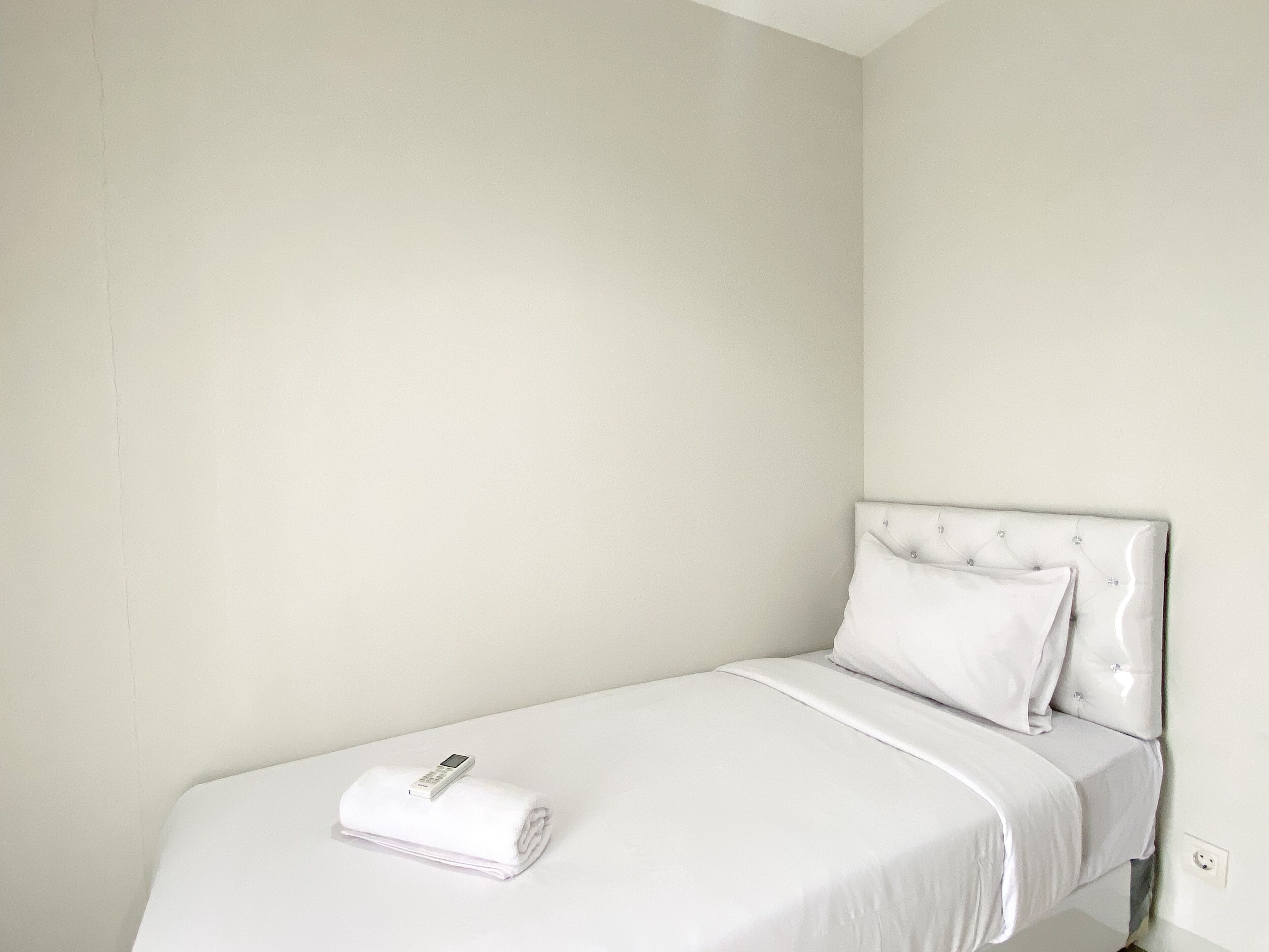 Un lit simple avec une tête de lit blanche et une serviette blanche soigneusement pliée posée dessus.