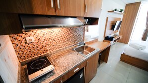 A compact kitchenette with a built-in stove, a sink, and a microwave. - Strategic And Homey Studio At Tamasari Papilio Apartment (Surabaya)