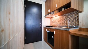 A modern kitchen with wooden cabinets, a black door, and a tiled backsplash. - Strategic And Homey Studio At Tamasari Papilio Apartment (Surabaya)