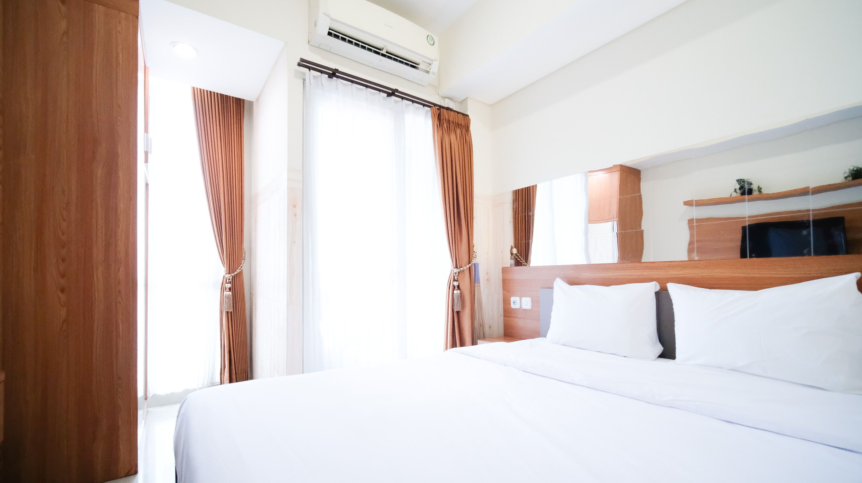 Ett hotellrum med en stor säng, en sänggavel i trä, en luftkonditioneringsanläggning och en liten köksvrå.