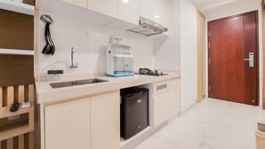 A modern kitchen with white cabinets, a built-in dishwasher, and a coffee machine. - Homey And Cozy Studio Sky House Bsd Apartment Near Aeon (Pagedangan)