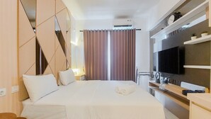 A hotel room with a bed, a TV, a desk, and a mirror. - Homey And Cozy Studio Sky House Bsd Apartment Near Aeon (Pagedangan)