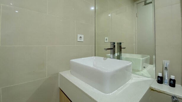 A modern bathroom with a white sink, a mirror, and a countertop with toiletries. - Spacious And Warm Studio Daan Mogot City Apartment (Jakarta)