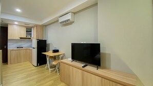 Een kleine keuken met houten keukenkastjes, een zwarte koelkast, een televisie op een houten dressoir en een eettafeltje met twee stoelen.