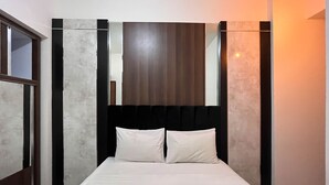 Un lit simple avec une literie blanche, dans une chambre dont la tête de lit est sombre et les murs clairs.
