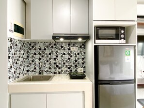 Compact kitchen with a stainless steel refrigerator, microwave oven, and sink, set against a black and white tiled backsplash.