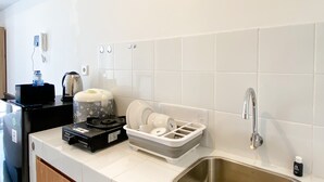 A kitchen with a stainless steel sink, a kettle, a coffee maker, and a dish rack. - Furnished Studio For 3 Pax With Sofa Bed At Tokyo Riverside Pik 2 Apartment (Teluknaga)