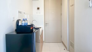 A compact kitchen with a refrigerator, a kettle, and a water dispenser. There is a door leading to a bathroom and a small window above the sink. - Furnished Studio For 3 Pax With Sofa Bed At Tokyo Riverside Pik 2 Apartment (Teluknaga)