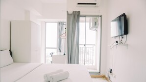 A hotel room with a bed, a TV, a window with curtains, and an air conditioning unit. - Gorgeous And Strategic Studio Apartment M-Town Residence (Gading Serpong)