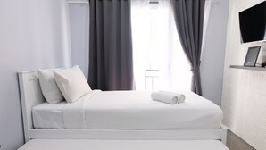 A modern hotel room with a neatly made bed, a flat-screen TV mounted on the wall, and a window with curtains.