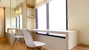Una habitación moderna con escritorio, dos sillas, ventanas amplias y un espejo.