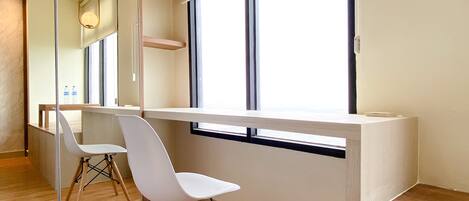 Une chambre moderne équipée d’un bureau et de deux chaises, de grandes fenêtres et d’un miroir.