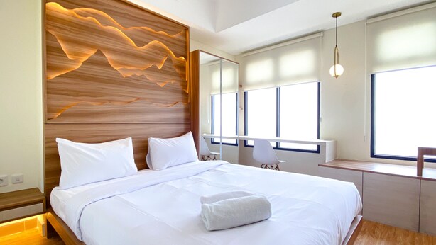 Una habitación de hotel moderna con una cama grande, cabecero de madera y vistas de la ciudad a través de amplias ventanas.