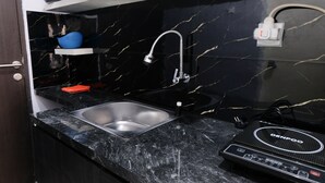 A kitchen with a black marble backsplash, a stainless steel sink, and a Genpo electric kettle on the counter. - Minimalist Studio At Grand Asia Afrika Apartment (Bandung)