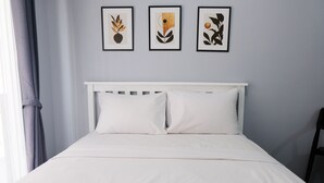 A neatly made bed with white bedding, a white headboard, and three framed artworks on the wall above. - Minimalist Studio At Grand Asia Afrika Apartment (Bandung)