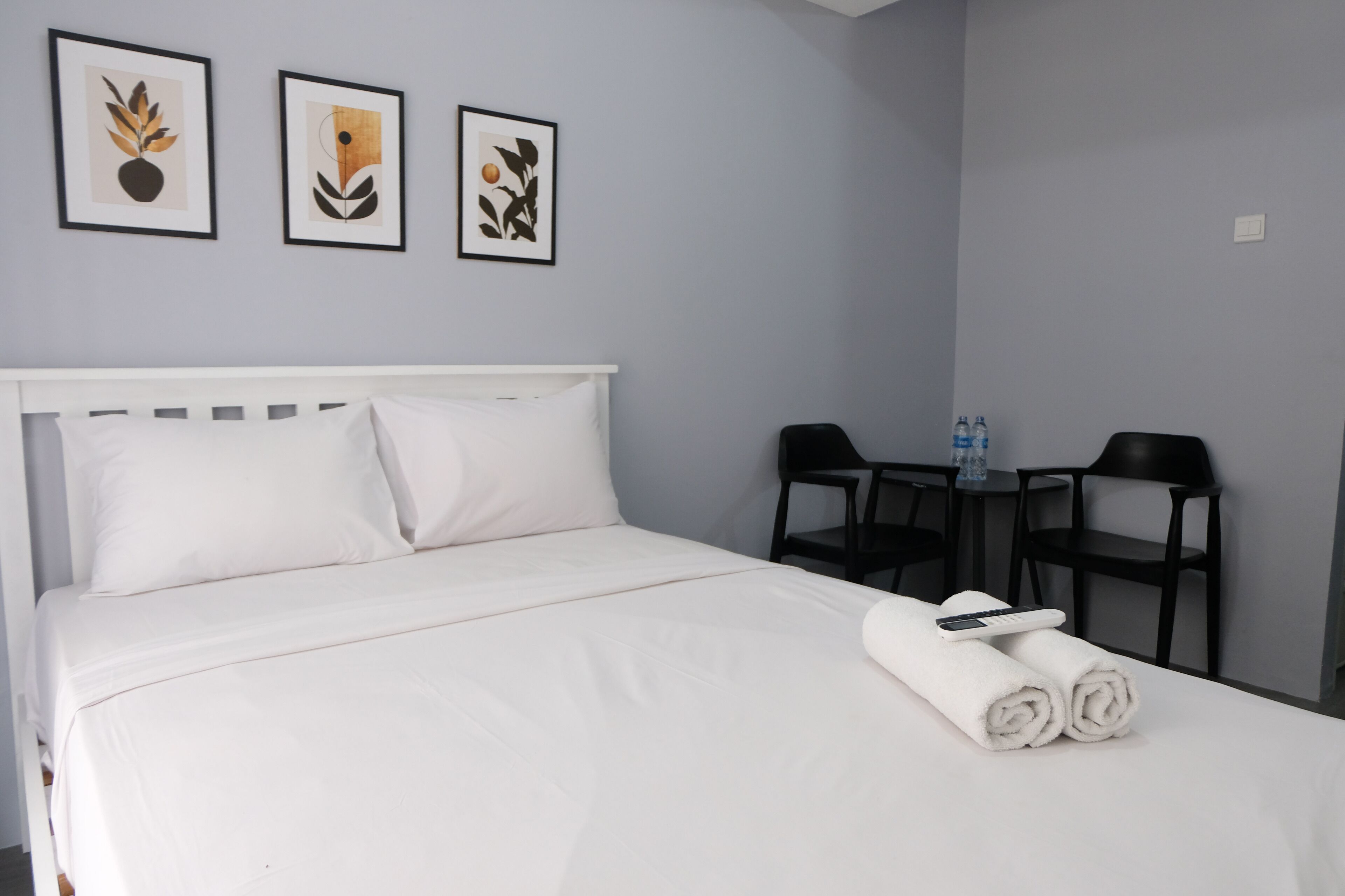 A neatly made bed with white linens, a white headboard, and two rolled towels on the bed. There are three framed artworks on the wall above the bed.