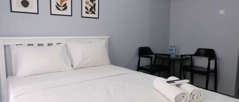 A neatly made bed with white linens, a white headboard, and two rolled towels on the bed. There are three framed artworks on the wall above the bed.