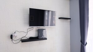 A modern room with a mounted TV, a power strip, and a speaker on a white brick wall. - Minimalist Studio At Grand Asia Afrika Apartment (Bandung)