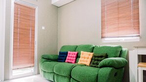 A green sofa with colorful cushions in a room with white walls and a window with blinds.