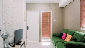 A living room with a green sofa, a white door, and a fan.