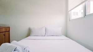 A neatly made bed with white linens and pillows, a wooden wardrobe, and a window providing natural light.