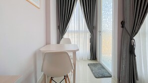 A dining area with a white table and chairs, a window with grey curtains, and a door with a patterned glass panel.