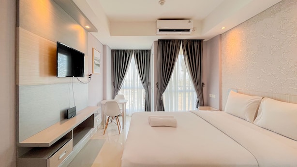 A modern hotel room with a large bed, a flat-screen TV mounted on the wall, a desk with a chair, and a window with curtains.