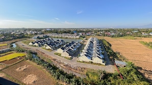 An aerial view of a residential area with modern houses arranged in rows, a small body of water, and surrounding agricultural fields.