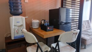 A small room with a water dispenser, a coffee maker, a travel bag, and a TV. There are two chairs and a sofa.