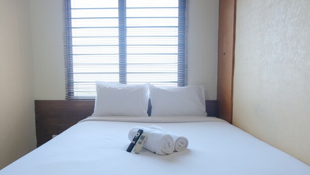 A neatly made bed with white linens, a rolled towel, and a remote control on the bed.