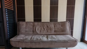 A brown sofa with metal legs in a room with a tiled floor and a wall with vertical wooden panels.
