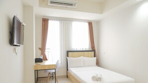 A bedroom with a bed, a desk, a chair, a TV, and a window with curtains. - Minimalist And Homey Studio At Evenciio Margonda Apartment (Depok)