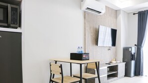 A modern kitchen with a microwave, refrigerator, and a flat-screen TV mounted on the wall. There is a wooden table with two chairs and a small cabinet below the TV. - Spacious And Homey Studio At Daan Mogot City Apartment (Jakarta)