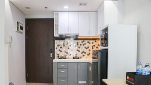 A compact kitchen with grey cabinets, a microwave, and a refrigerator. There is a small table with water bottles on it. - Spacious And Homey Studio At Daan Mogot City Apartment (Jakarta)