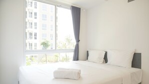 Una habitació d'hotel amb un finestral gran, un llit amb roba blanca i un capçal de llit gris.