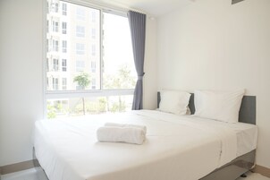 Una habitación de hotel con un ventanal grande, una cama con sábanas blancas y un cabecero gris.