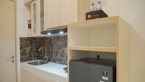 A compact kitchen with a double sink, a refrigerator, and wooden cabinets. - Minimalist And Comfy Studio At Tokyo Riverside Pik 2 Apartment (Teluknaga)