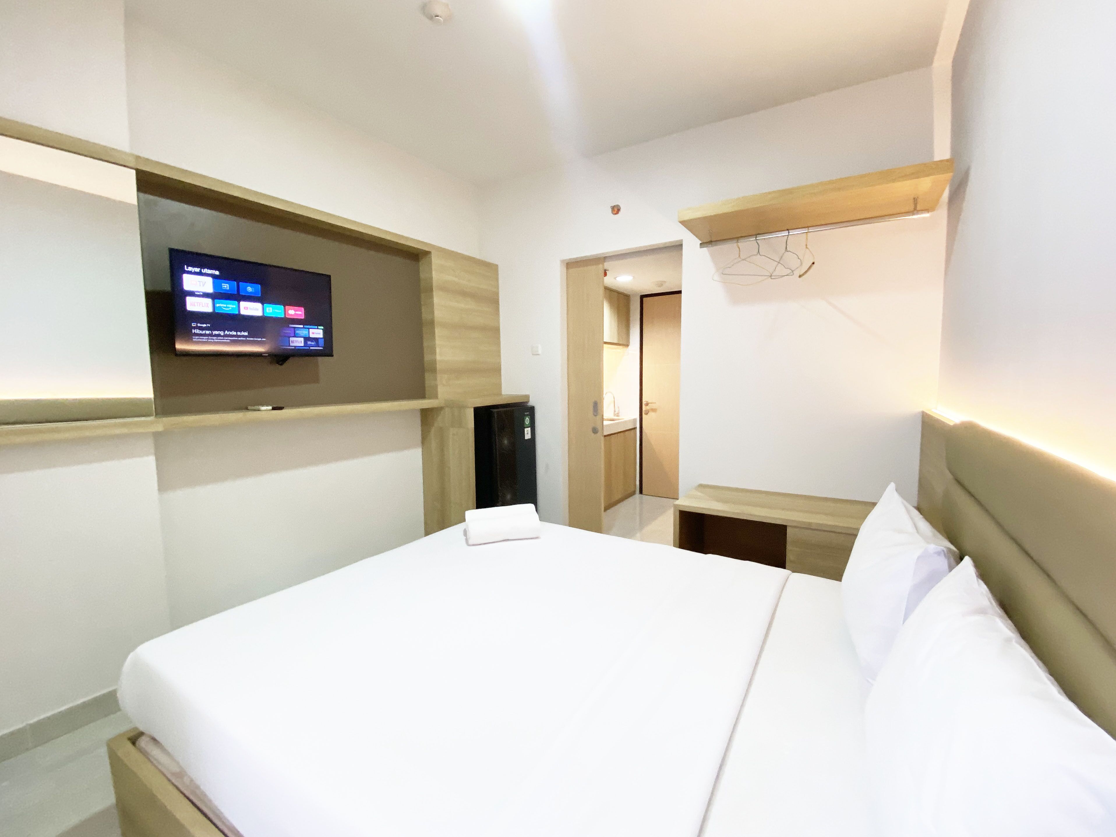 Una habitación de hotel con una cama, un televisor montado en la pared, un escritorio y un espejo.