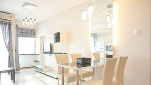 Un espace de salle à manger moderne avec une table en verre, des chaises blanches et des luminaires suspendus.