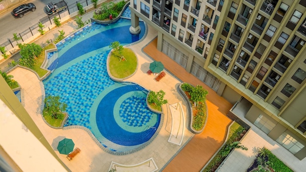 An aerial view of a residential building with a swimming pool, a children's slide, and a small park area with benches and trees.