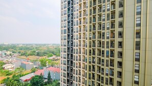 A high-rise building with multiple balconies and a view of a residential area with houses and greenery.